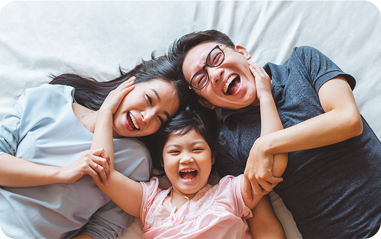 Asian parents with daughter laying on sheet looking up at camera smiling
