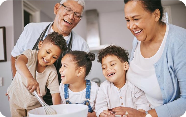 Grandparents in kitchen with grandchildren mixing something in a bowl