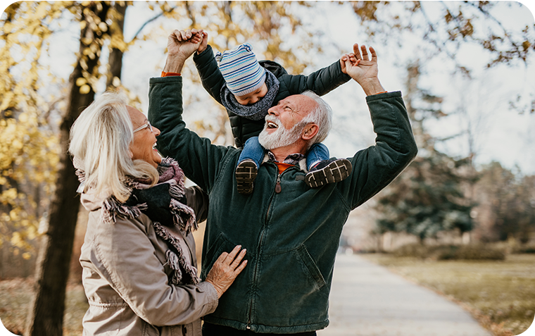 Happy grandparents walking in park with grandson on shoulders