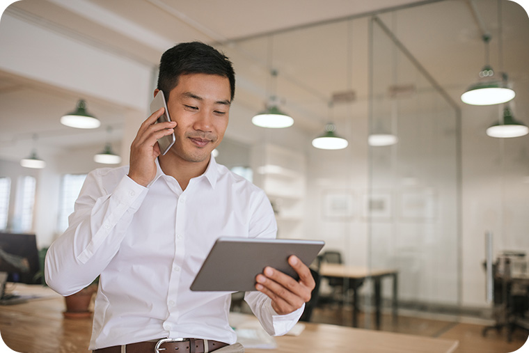 Young Asian businessman on phone looking at tablet
