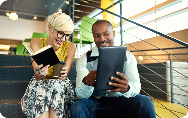 Woman with book looking at tablet with male colleague